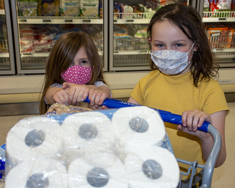 Two little girls at the Dugway Commissary wear masks while they help Mom with grocery shopping May 11. Photo by Al Vogel, Dugway Public Affairs