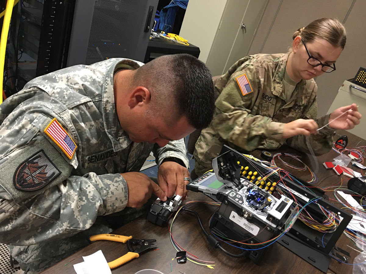 Cable installers Sgt. Geraldo Benavides and Spc. Amber Rudd cut fiber cable to prepare it for splicing, using an arc fusion splicing apparatus, which basically sparks and melds two fiber ends. (Photo by Michael Novogradac, USAOTC Public Affairs)