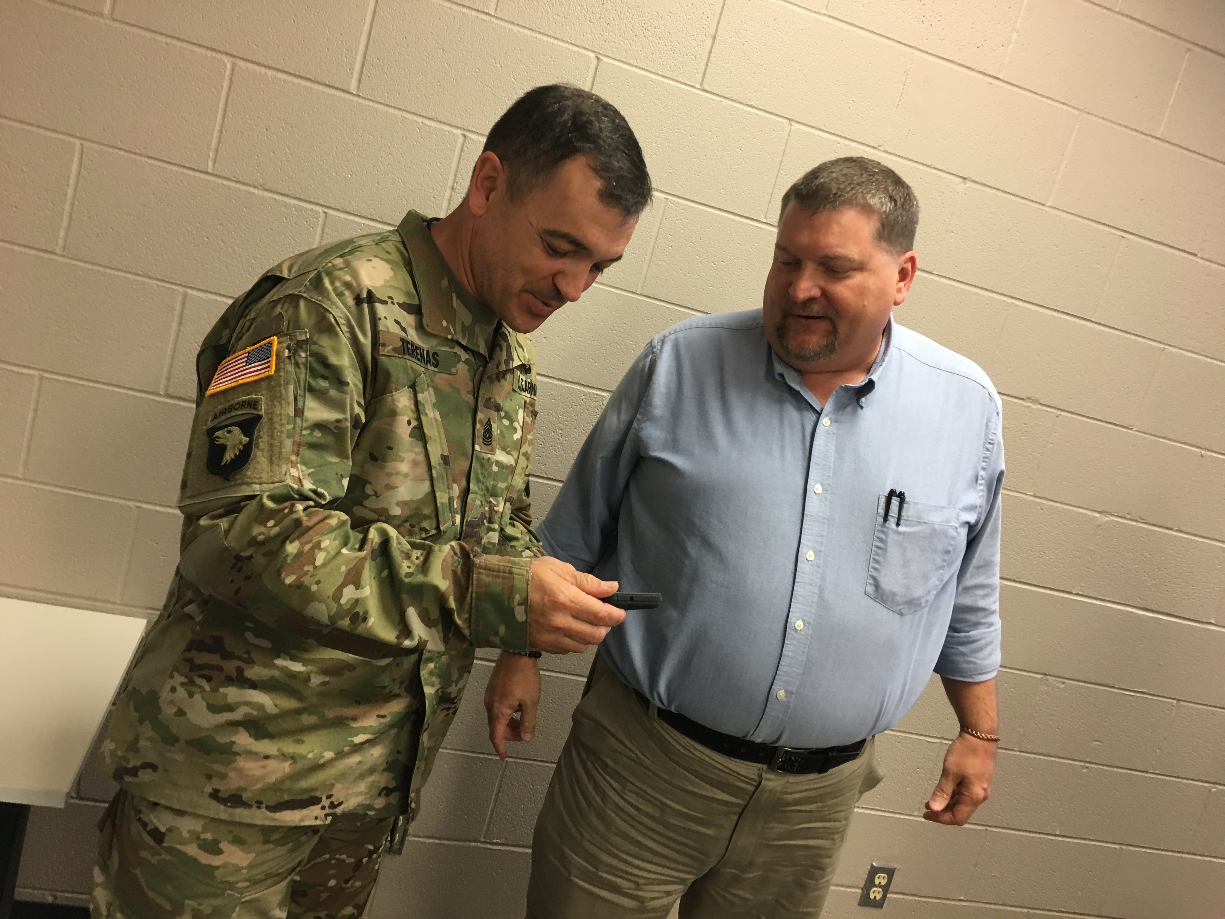 U.S. Army Operational Test Command Command Sgt. Maj. Mario O. Terenas, and Florence, Texas High School Principal Steven Elder, share memories on Elders cell phone from their times deployed 
