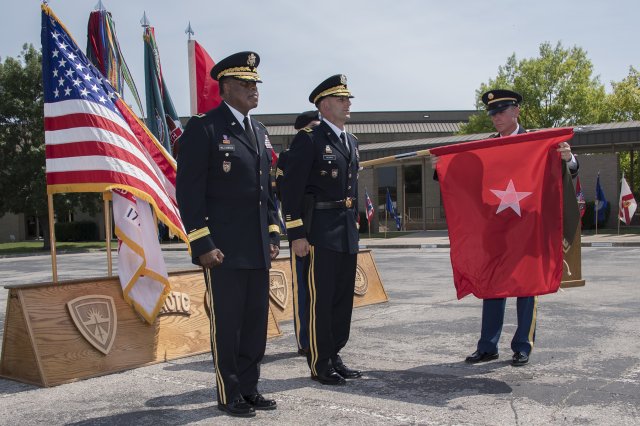 Command Sgt. Maj. Jason Schmidt (right) uncases the Army's newest one-star general officer flag after Col. John C. Ulrich (center) is promoted to briagadier general (Photo Credit: Larry Furnace)
