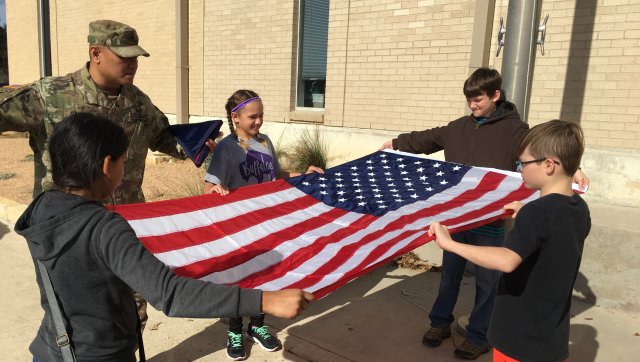 Sgt. 1st Class Benito Santos, a research development test and evaluation non-commissioned officer in Operational Test Command's Maneuver Test Directorate, trains fifth-graders how to unfold the flag at Florence Elementary School, Florence Texas, on Jan. 20, 2017. (Photo Credit: Mr. Michael M Novogradac (Hood))